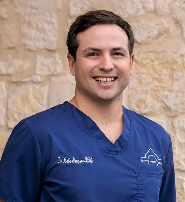 Dr. Cole Simpson, DDS, in navy Boerne Dental Center scrubs against a limestone wall.