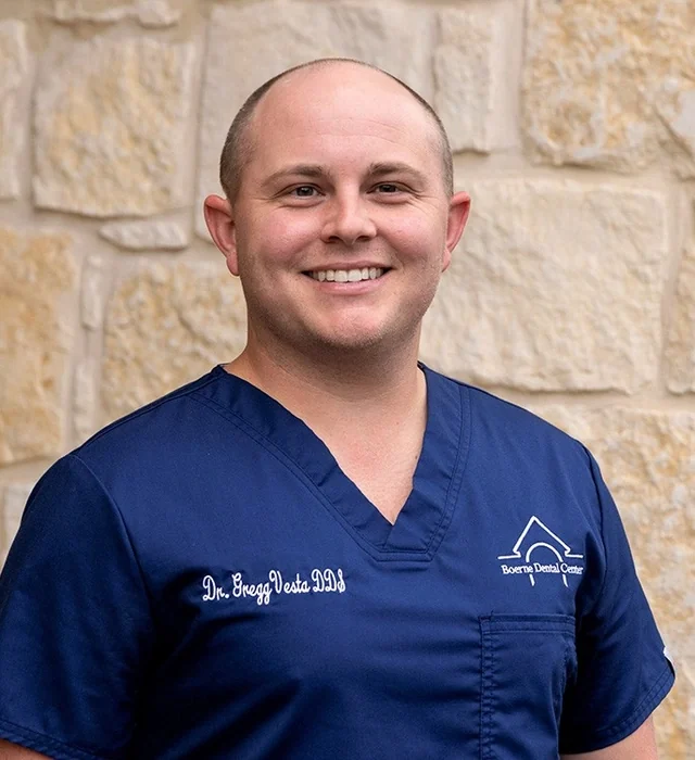 Dr. Gregg Vesta II, DDS, in navy Boerne Dental Center scrubs against a limestone wall.