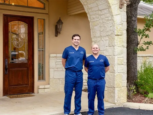 Dr. Simpson and Dr. Vesta at the carved wooden front door, under the stone arch of the entrance.