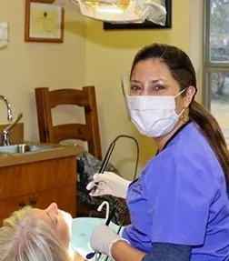 A Boerne Dental Center team member in a purple gown and mask, at work with a patient.