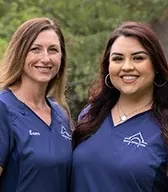 Two team members in navy scrubs with the practice's roof logo, outdoors.