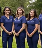 Boerne Dental Center team members in navy scrubs, outdoors under the oaks.