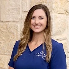 Laura, Office Manager at Boerne Dental Center, in navy scrubs against a limestone wall.