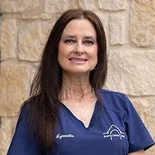 Lynnette, Registered Dental Hygienist at Boerne Dental Center, in navy scrubs against a limestone wall.