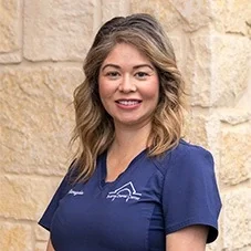 Nereyda, Registered Dental Assistant at Boerne Dental Center, in navy scrubs against a limestone wall.