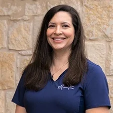 Sarah, Registered Dental Assistant at Boerne Dental Center, in navy scrubs against a limestone wall.
