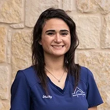 Shelby, Registered Dental Assistant at Boerne Dental Center, in navy scrubs against a limestone wall.