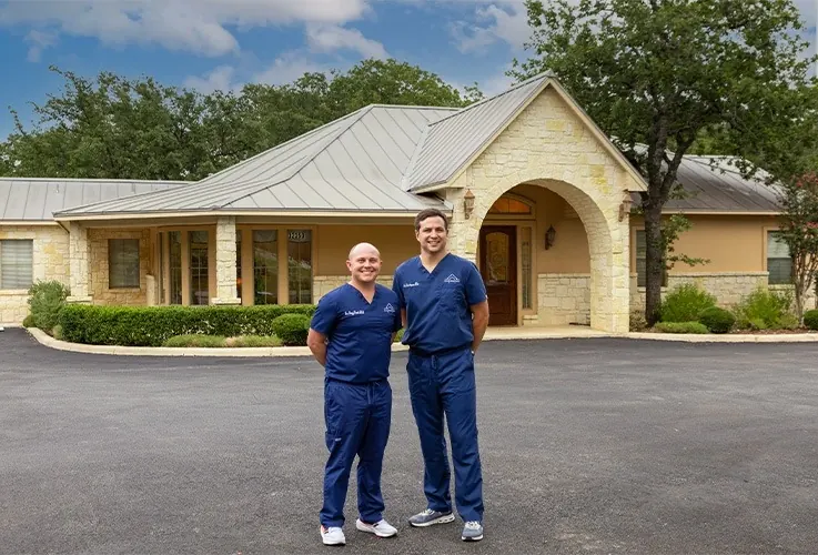 Dr. Simpson and Dr. Vesta in the car park in front of the stone Boerne Dental Center building.